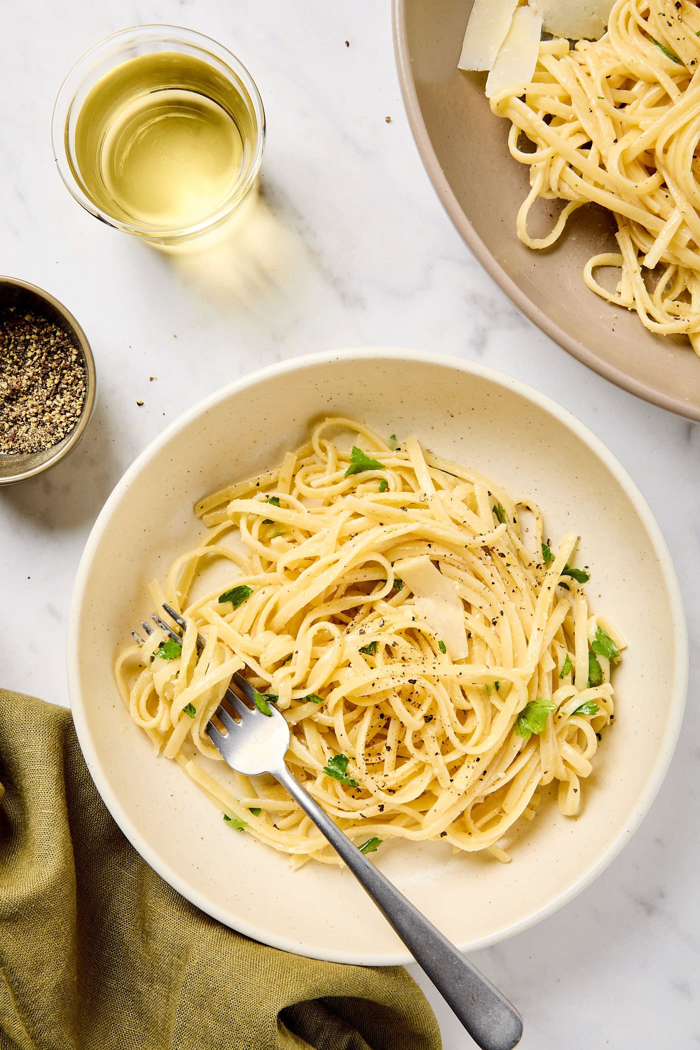 A bowl of lemon butter pasta in a bowl topped with parsley and black pepper.