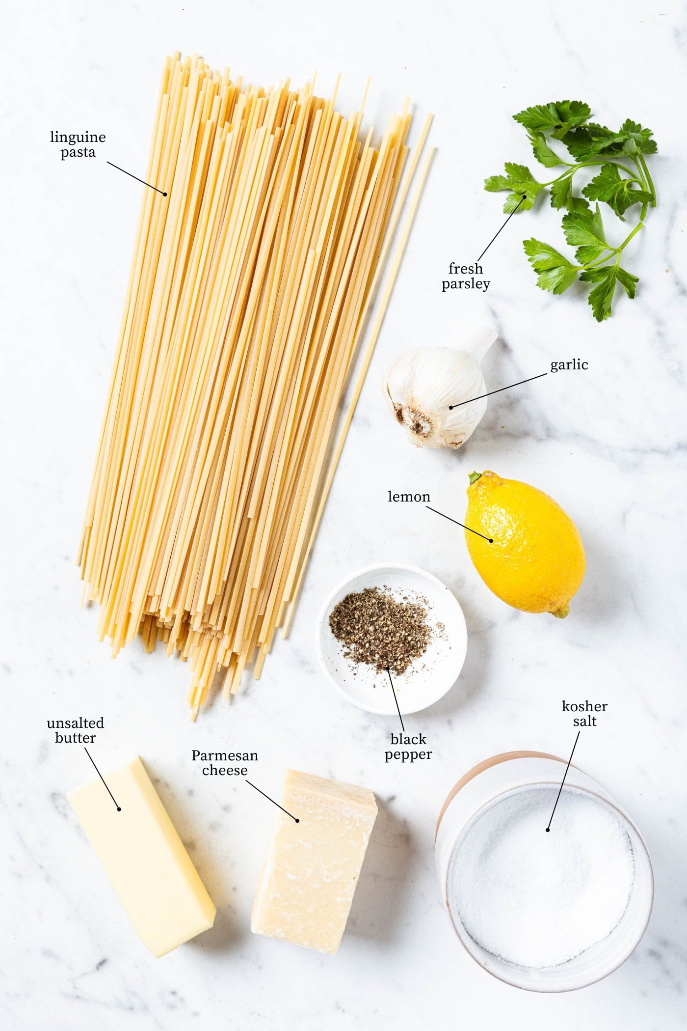 White marble surface with ingredients for butter pasta recipe including linguine, lemon, garlic, butter, and more.