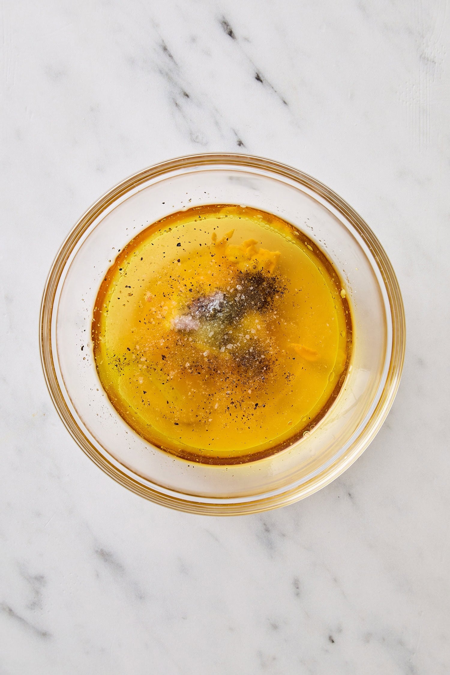 Glass bowl on marble surface with unmixed ingredients for a vinaigrette.