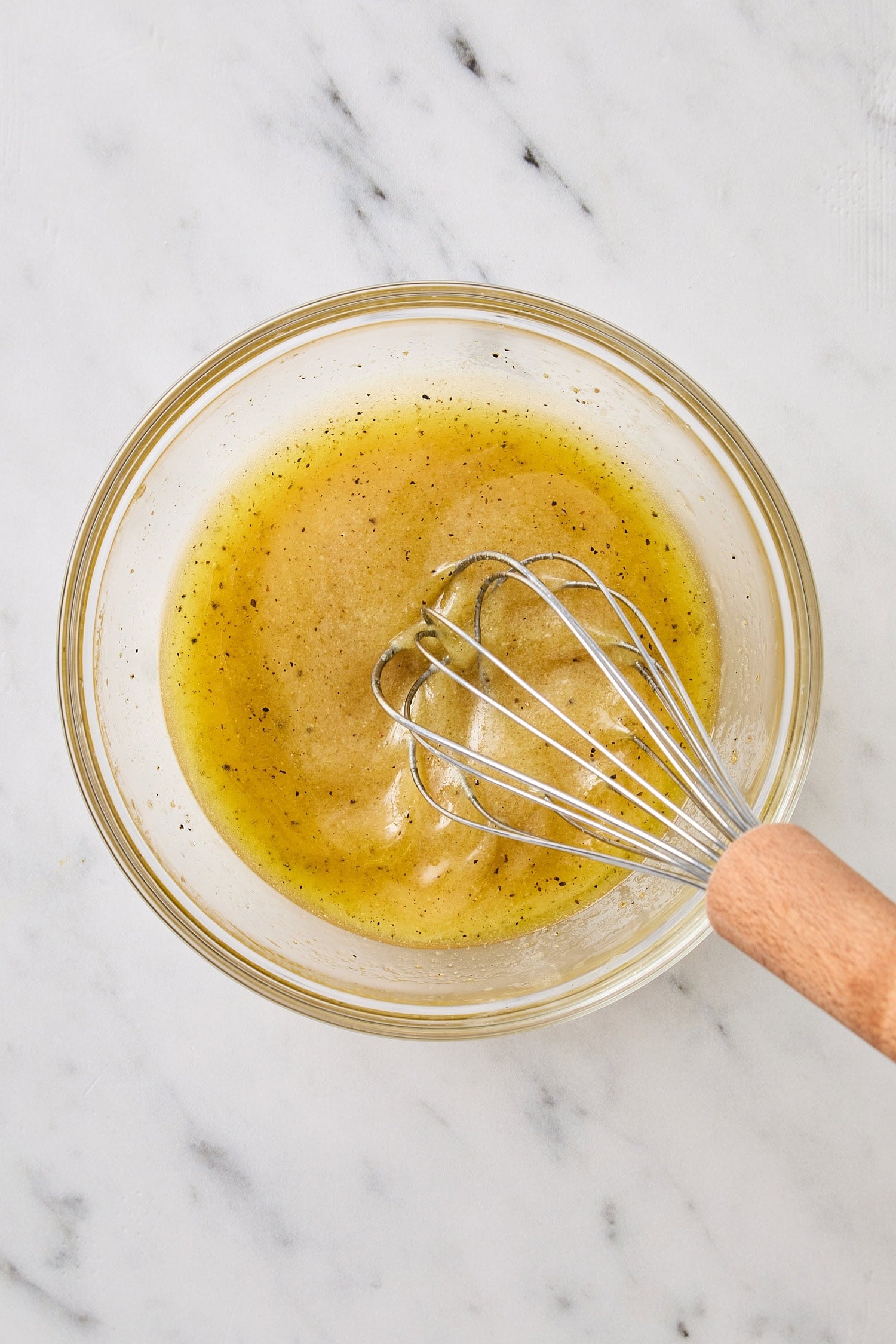 Glass bowl with yellow colored vinaigrette being mixed with a whisk.