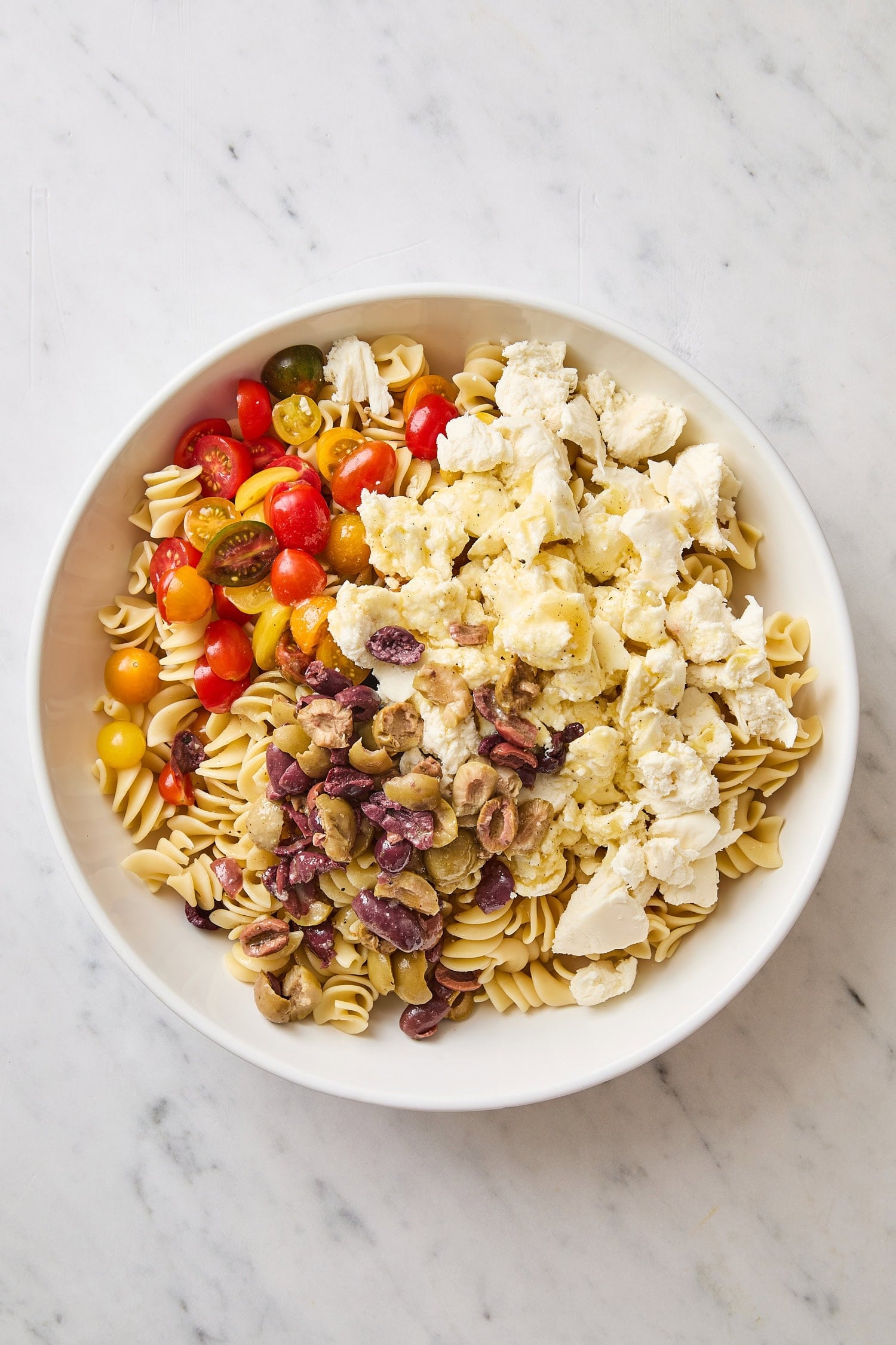 White bowl filled with pasta, tomatoes, fresh mozzarella for Caprese pasta salad.