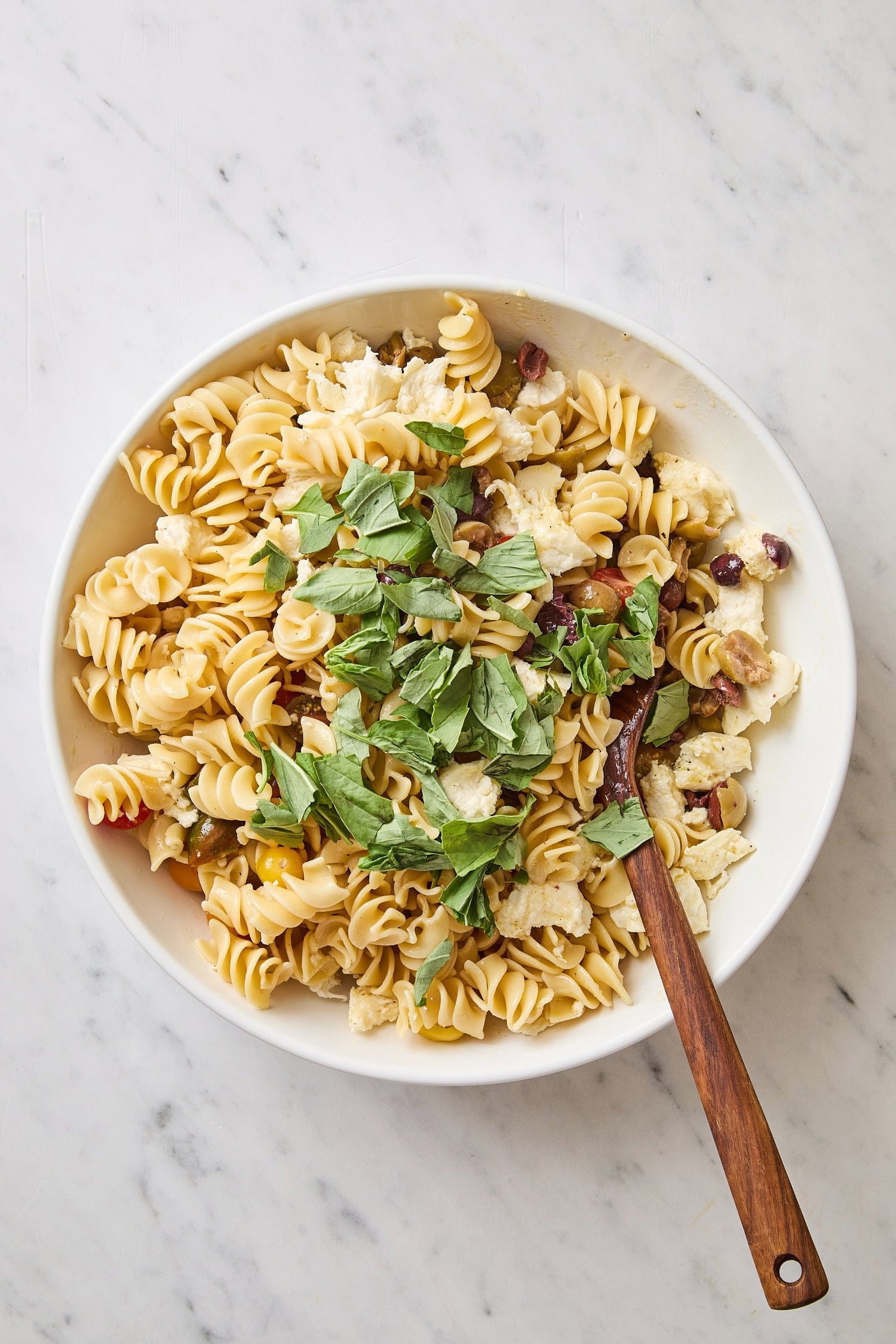 Fresh basil torn on top of Caprese pasta salad.