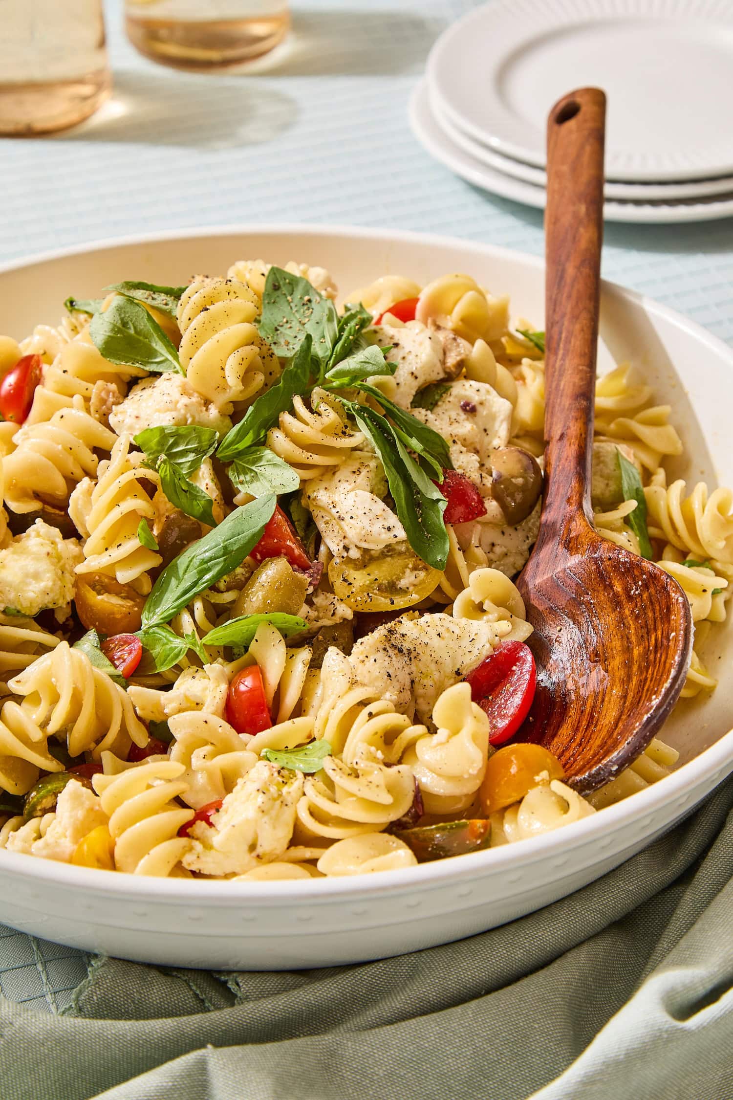 White bowl filled with pasta salad with sliced cherry tomatoes and fresh basil.
