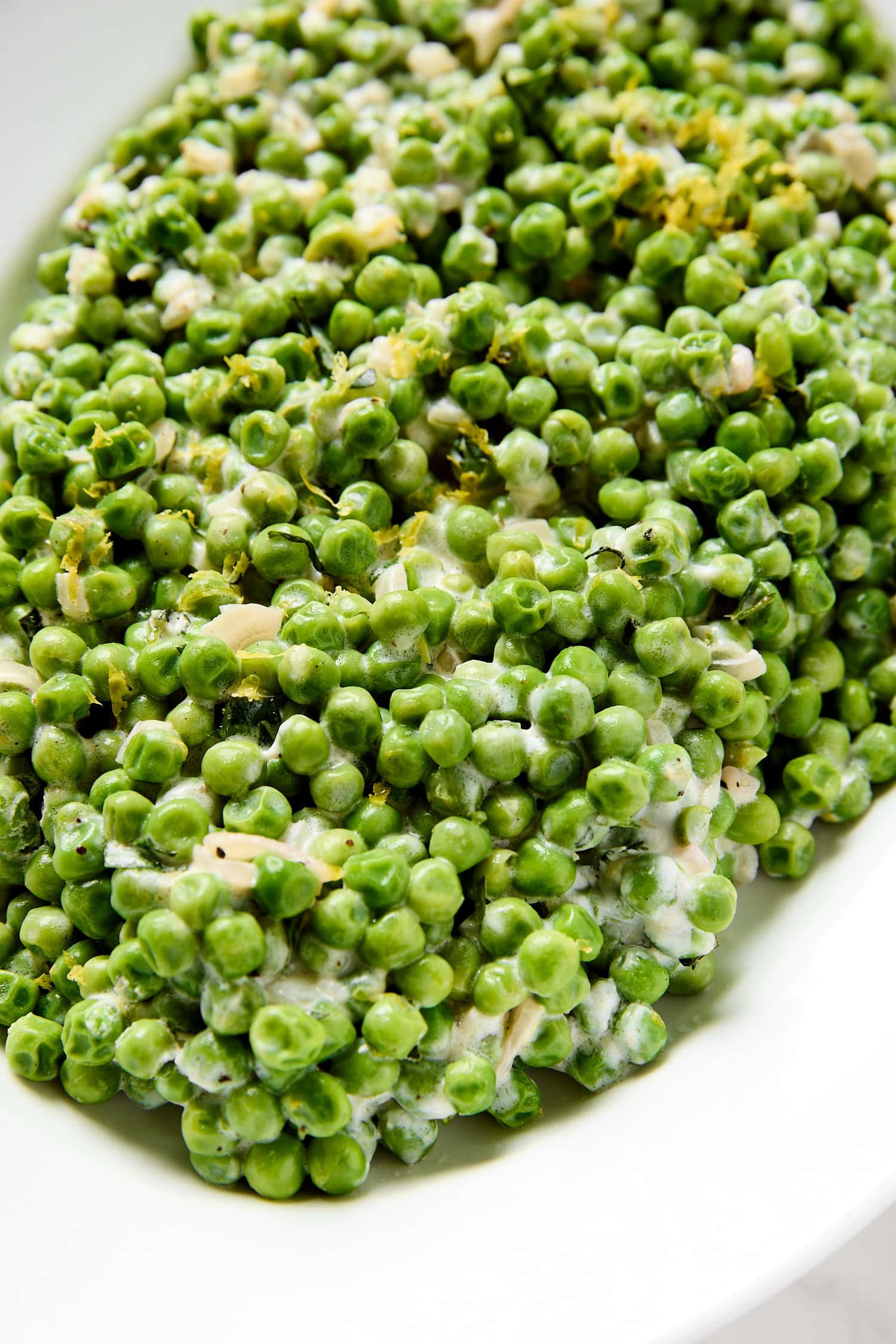 White platter filled with bright green peas with lemon zest sprinkled on top.
