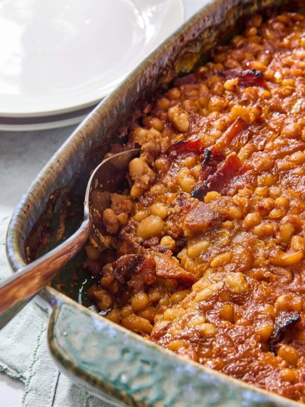 Green pan with baked beans with spoon scooping out a serving.
