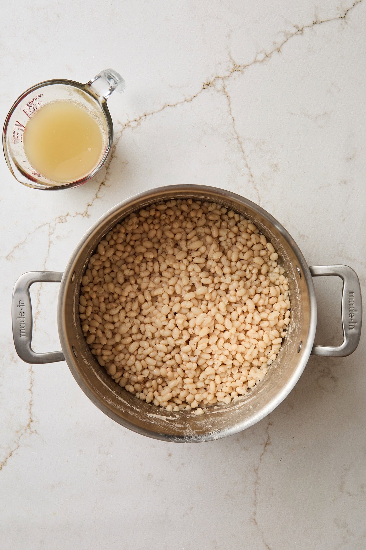 Saucepan filled with cooked beans with extra cooking liquid reserved.