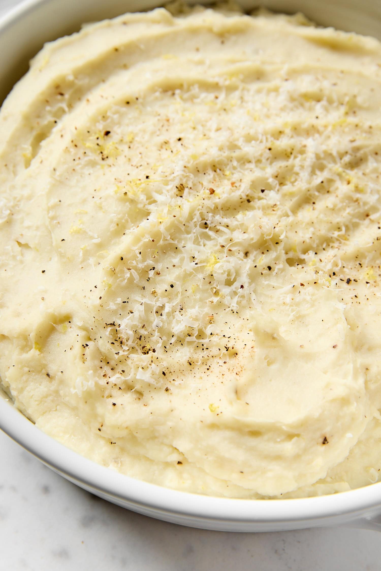 White bowl filled with lemon ricotta mashed potatoes with a sprinkle of lemon zest on top.