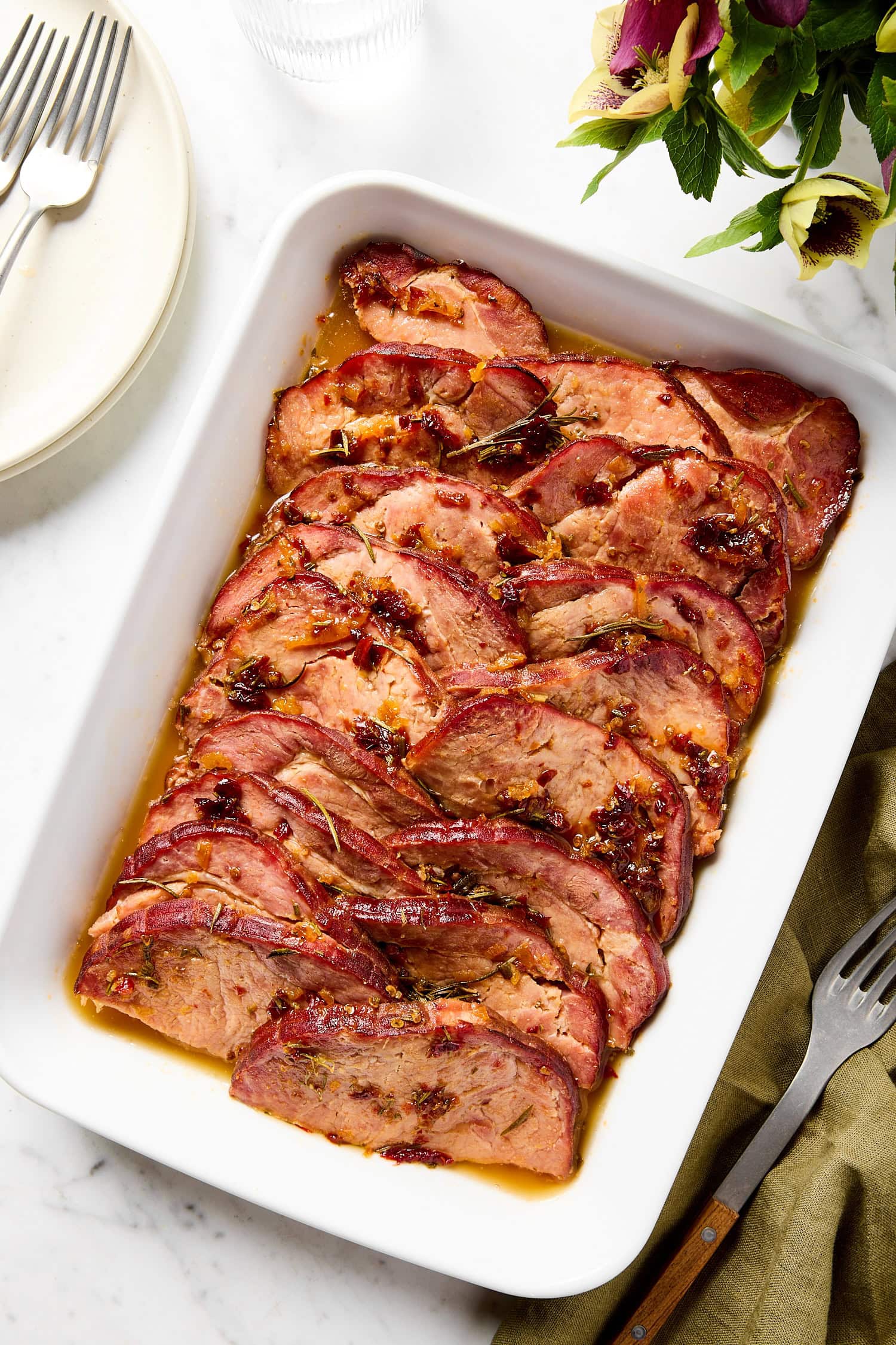 White baking dish filled with orange chipotle glazed ham with glaze on top.