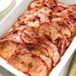White baking dish with slices of glazed ham with chipotle glaze on top.