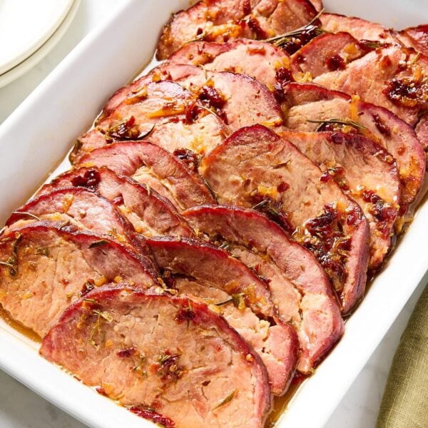 White baking dish with slices of glazed ham with chipotle glaze on top.