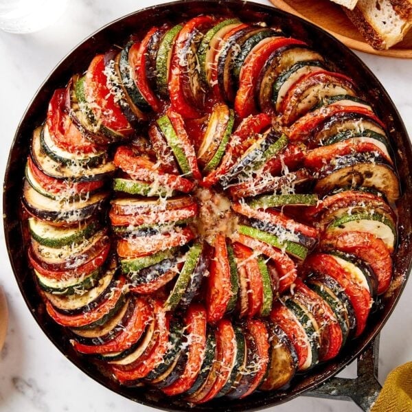 Black skillet with cooked ratatouille with Parmesan cheese on top.