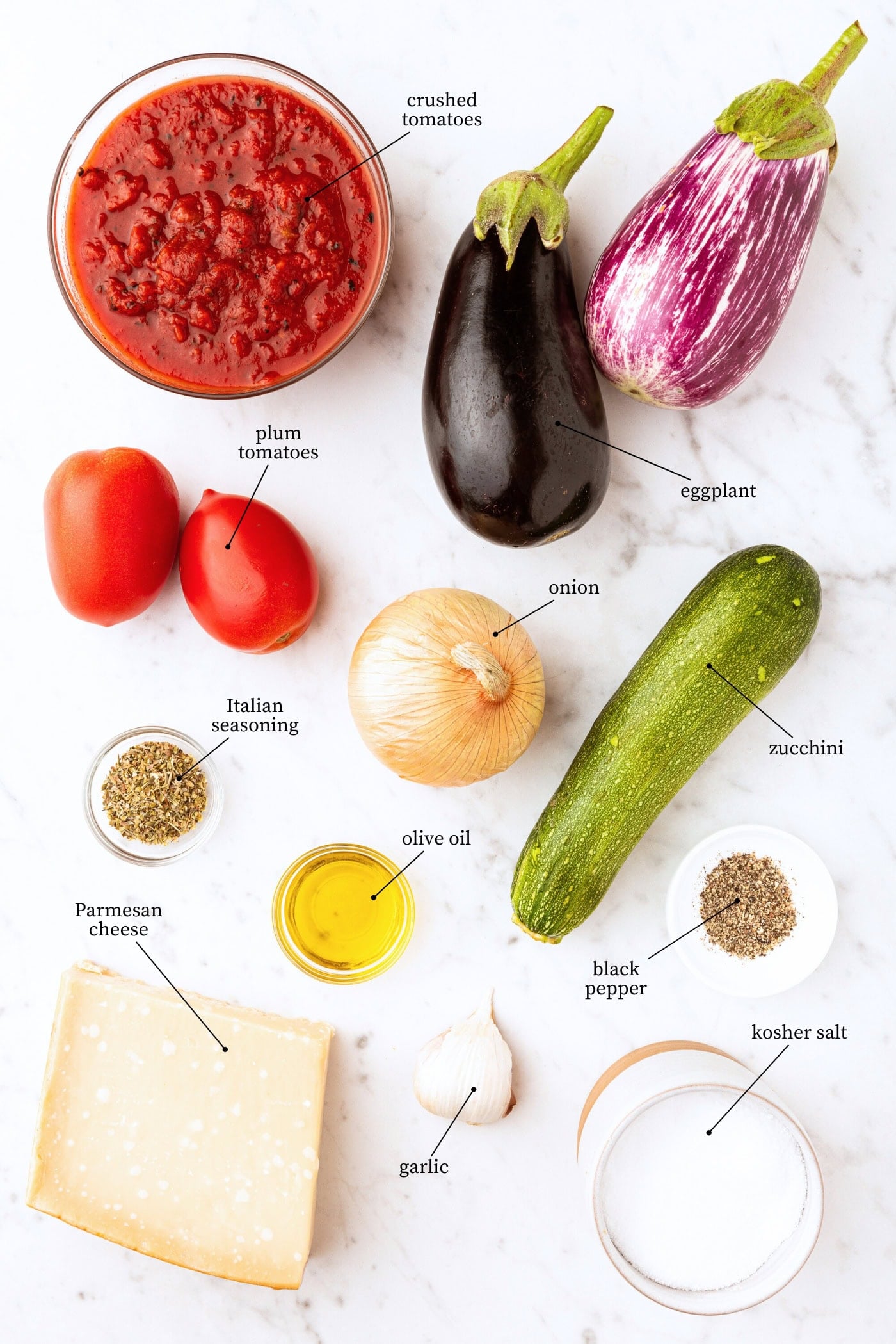 White marble surface filled with ingredients for ratatouille including eggplant, tomatoes, sauce, and more.