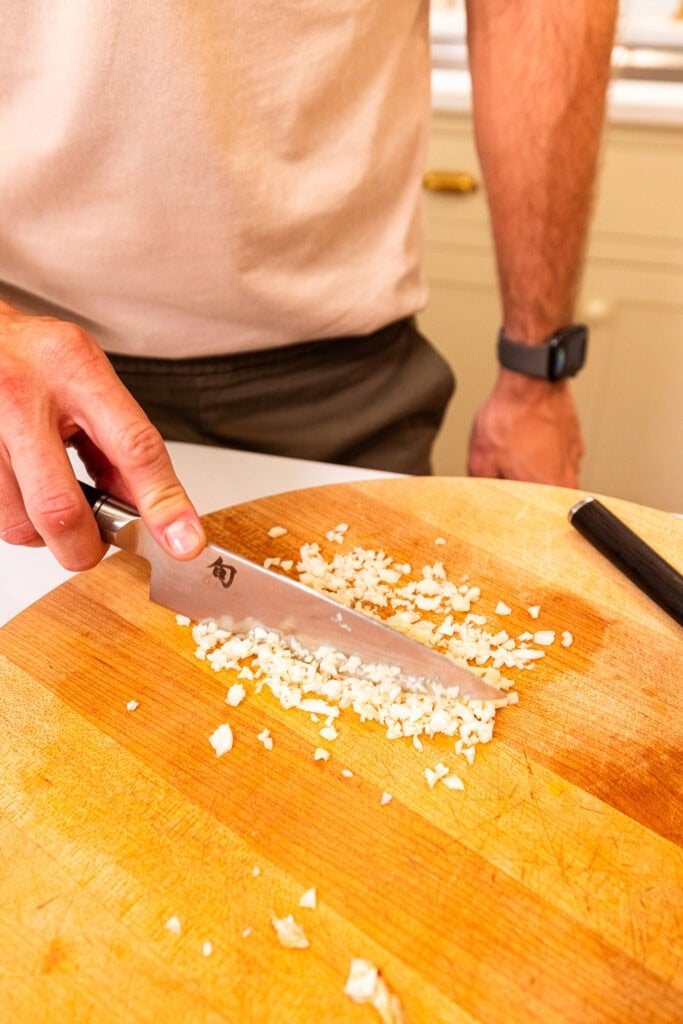 Hand chopping up garlic into a fine mince with a knife.