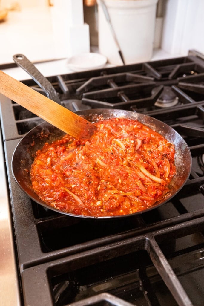 Wooden spatula mixing together tomato sauce with pieces of onions.