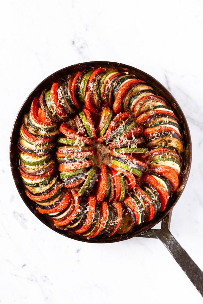 Skillet with cooked ratatouille on white marble surface after cooking.