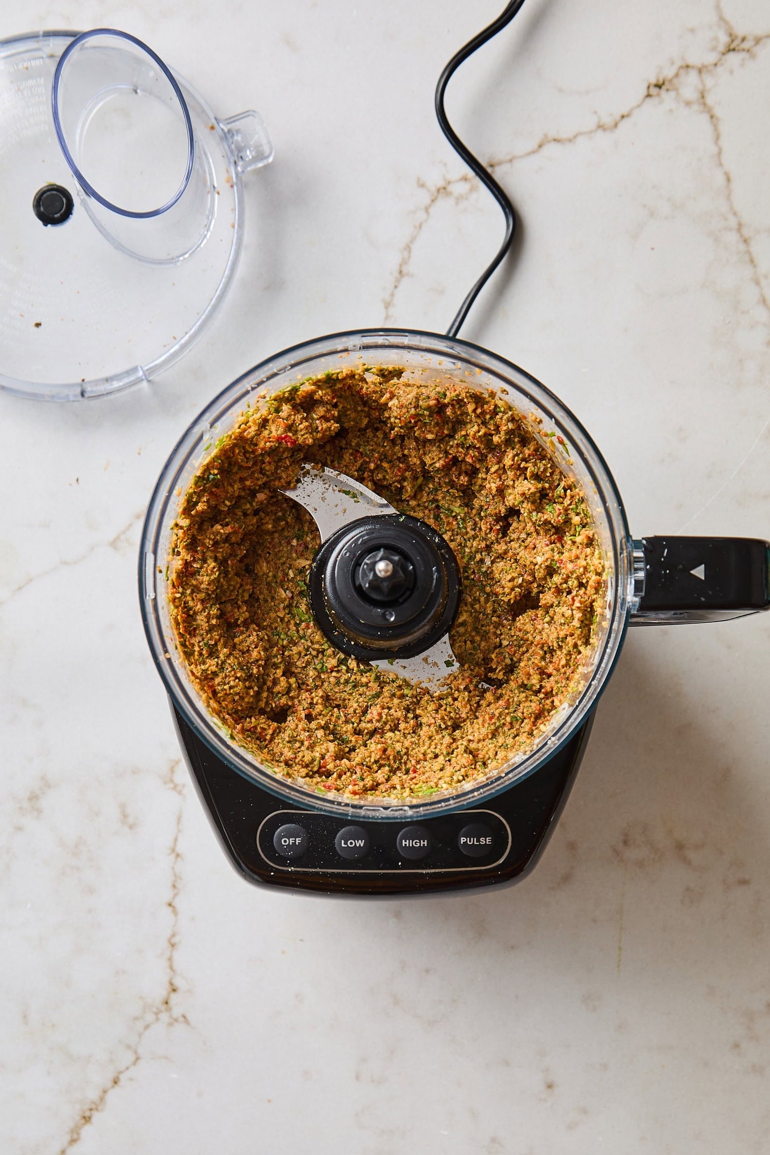Food processor with blended ingredients for arugula pesto.