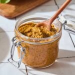Glass jar filled with orange colored arugula pesto with spoon scooping out some.
