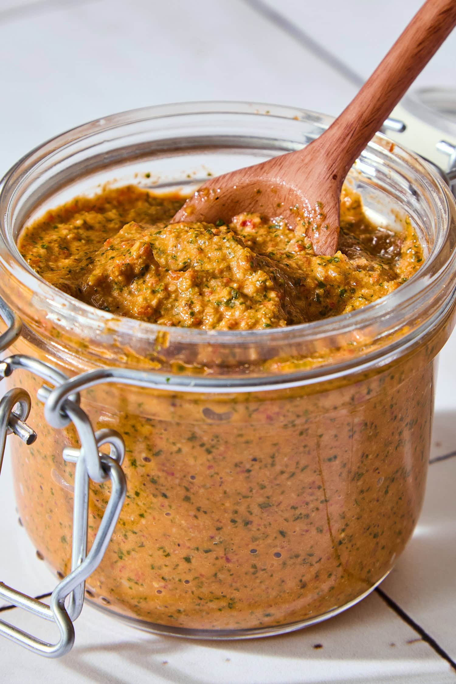 Glass jar with wooden spoon scooping up a portion of arugula pesto.