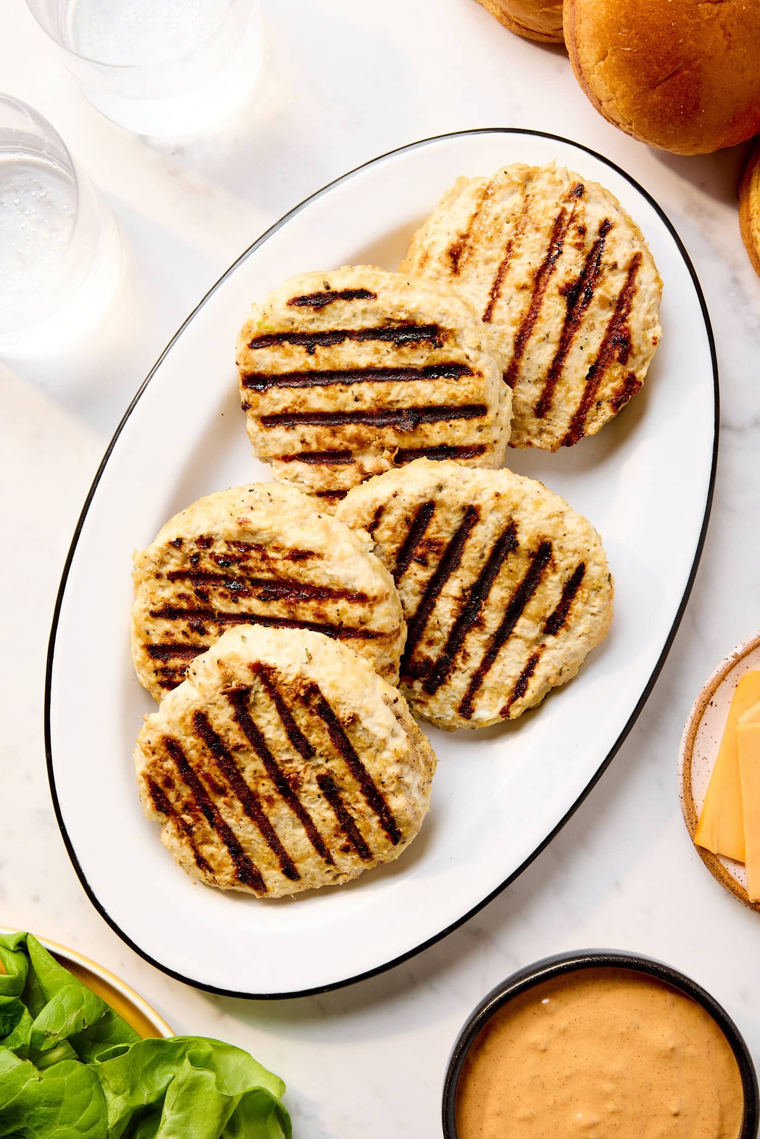 Grilled chicken burgers on a plate with lettuce and sauce on the side.
