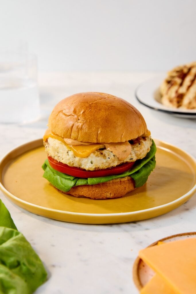 A chicken burger with lettuce, tomato, and sauce sits on a plate.