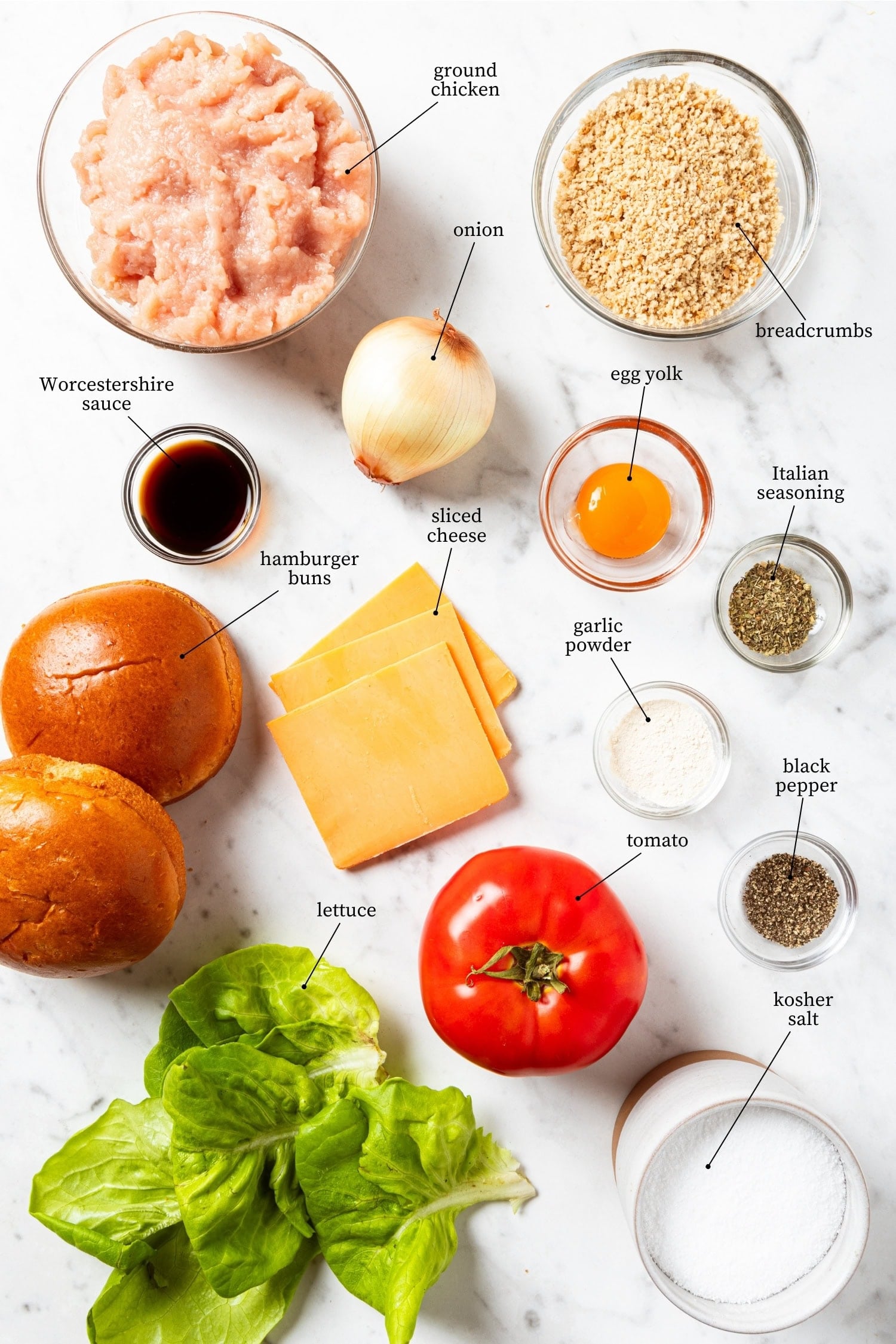 White marble surface filled with ingredients needed for grilled chicken burgers including meat, breadcrumbs, and more.