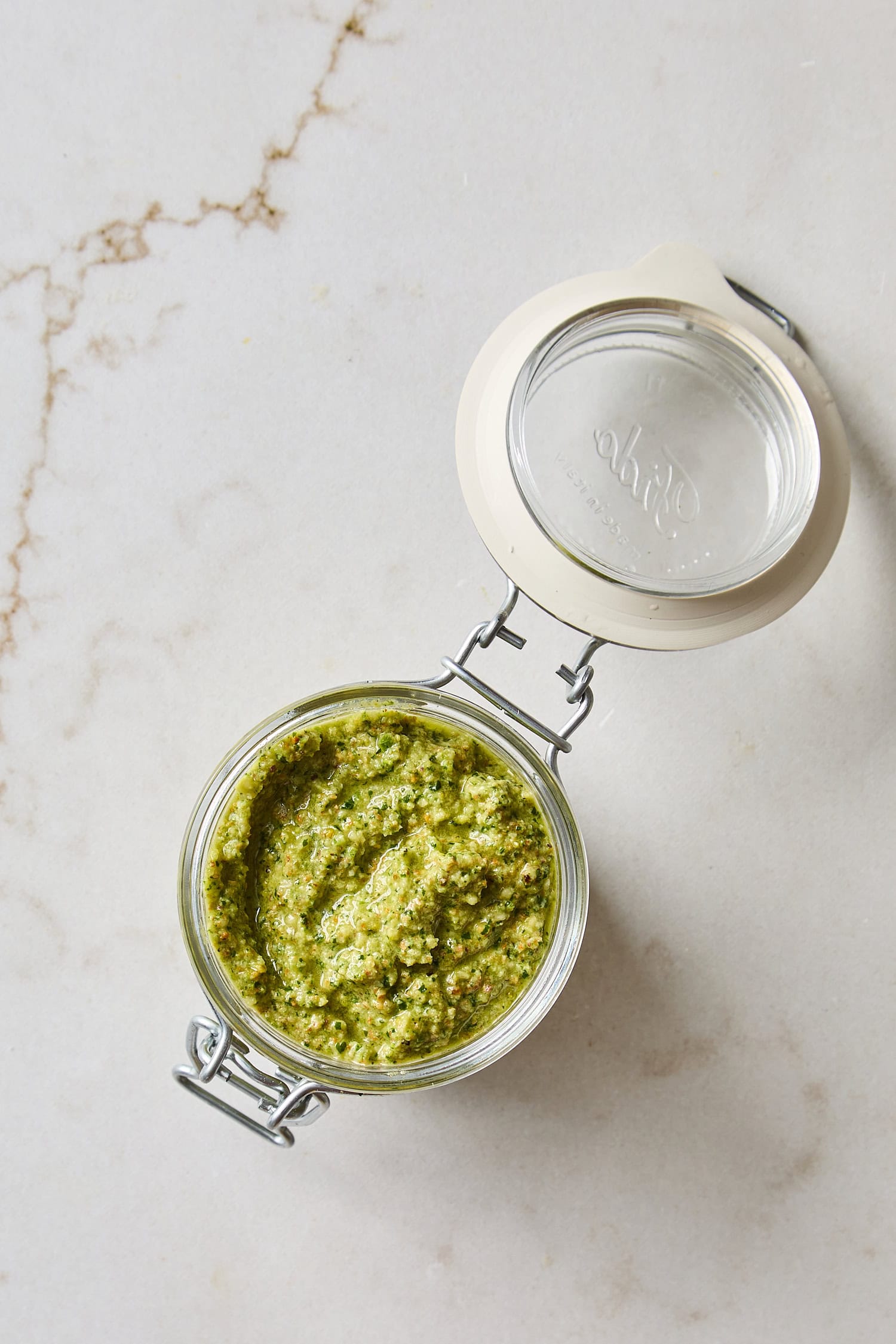 White countertop with glass container filled with green colored pesto.