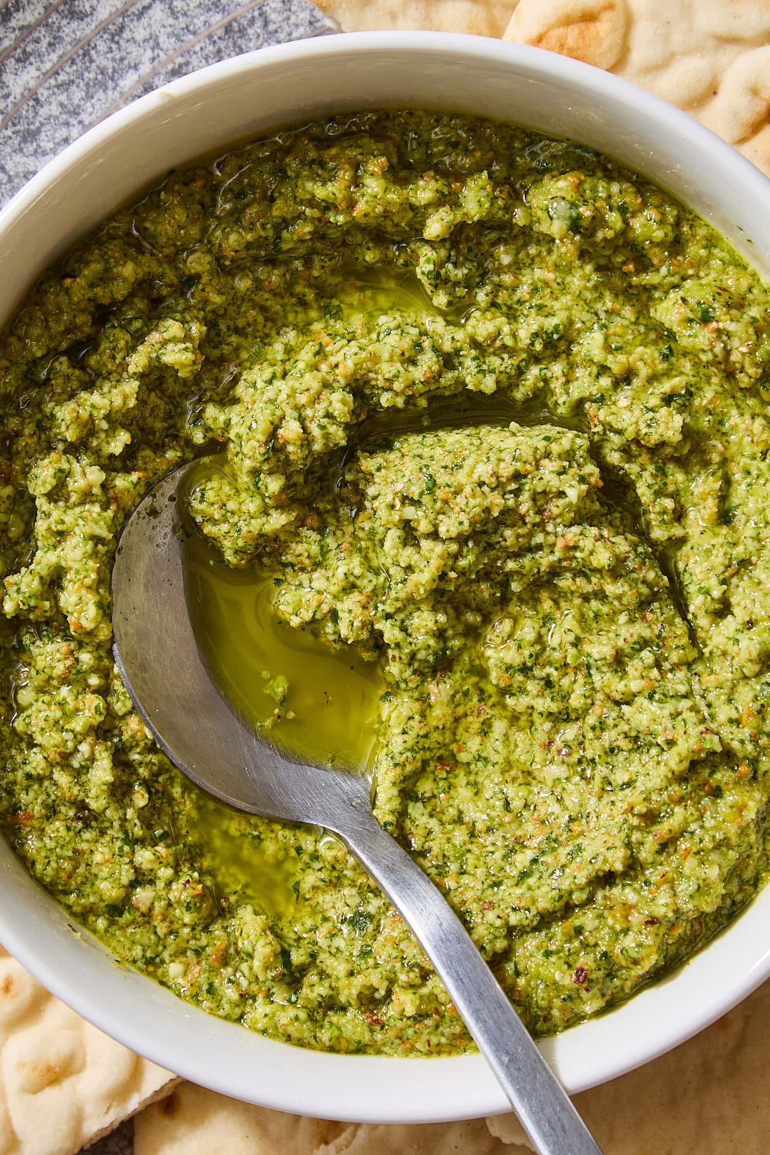 Bowl with cilantro pesto with spoon scooping up a serving with olive oil showing.