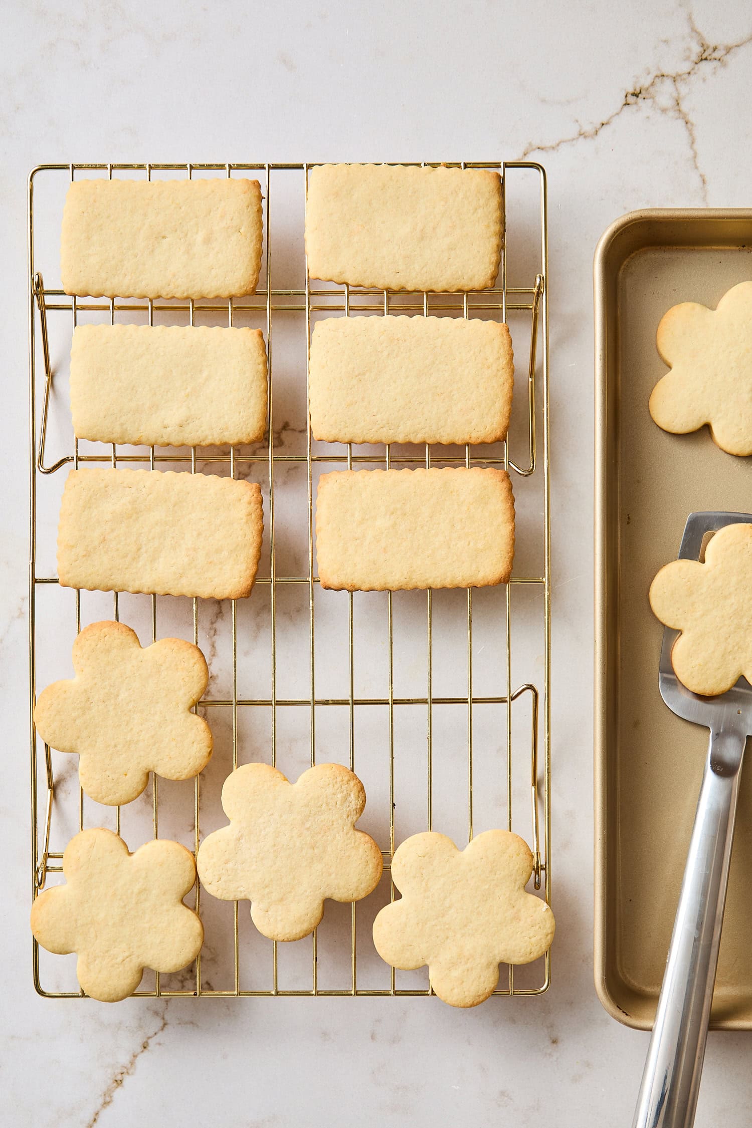 Baked sugar cookies on cooling rack being taken off of baking sheet.