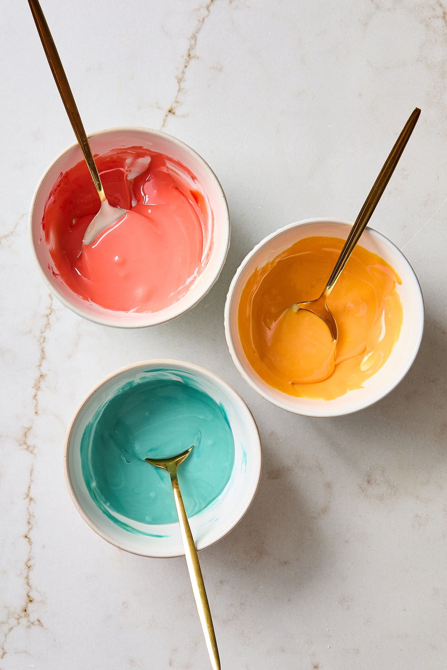 Three bowls of colored royal icing for sugar cookies.