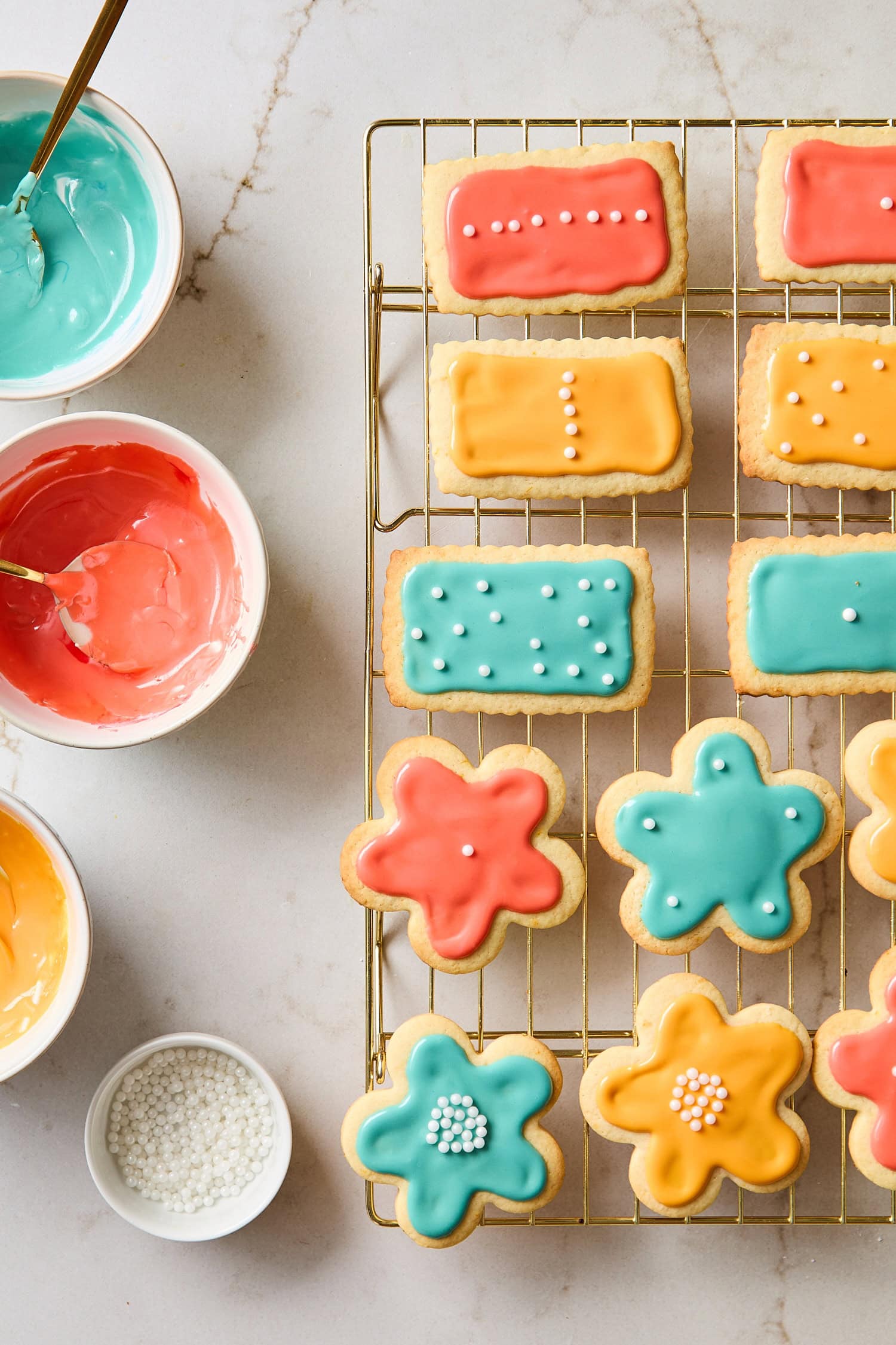 Bowls of colored royal icing frosting cookies on cooling rack.