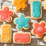 Cooling rack with frosted sugar cookies with orange, blue, and pink frosting.