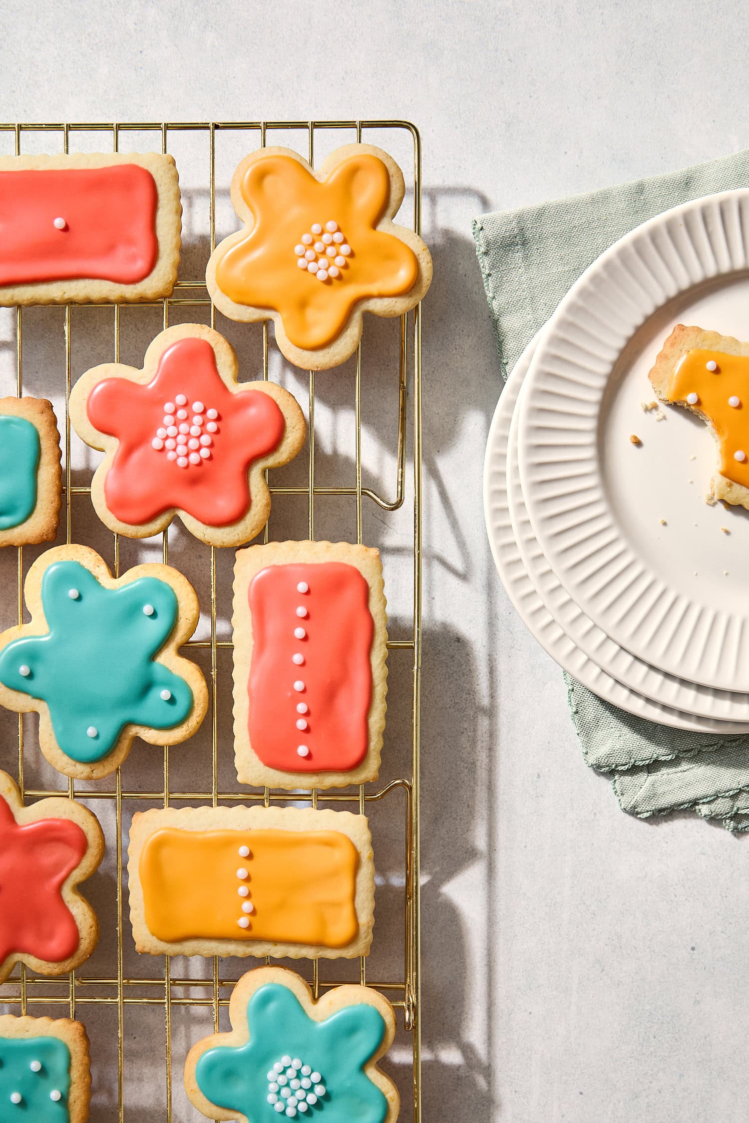 Frosted sugar cookies on a cooling rack with one cookie on a plate with a bite taken out.