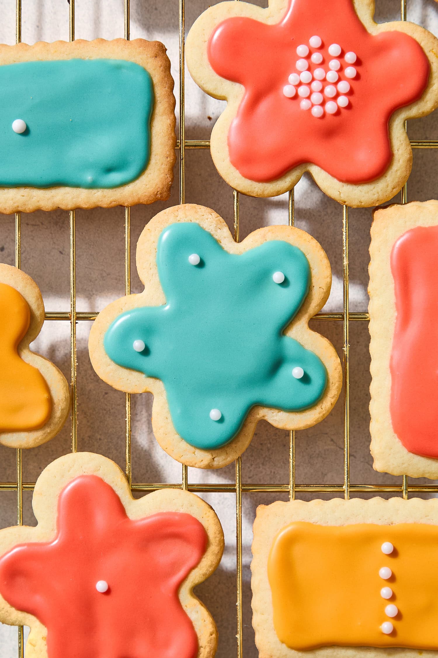 Frosted cutout sugar cookies on a cooling rack with colored frosting on top.