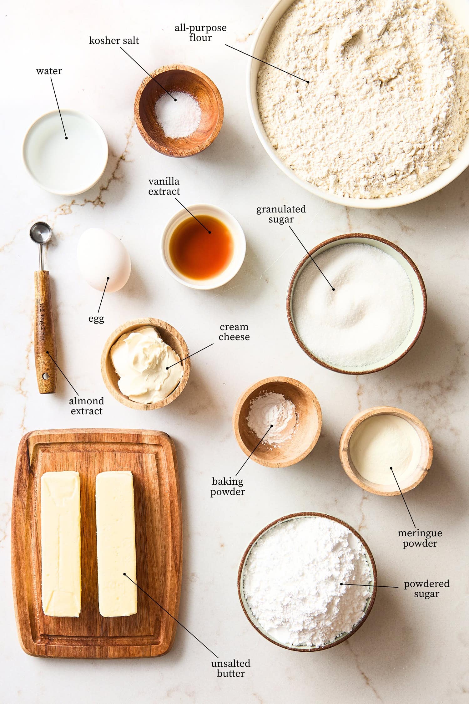 White surface with ingredients for cutout sugar cookies including butter, sugar, flour, and more.
