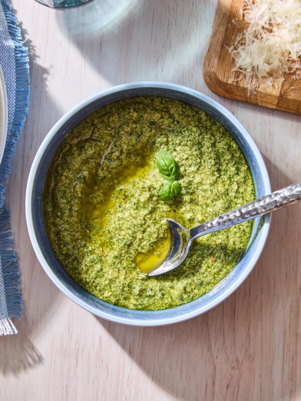 Blue bowl filled with fresh basil pesto recipe with two basil leaves on top.