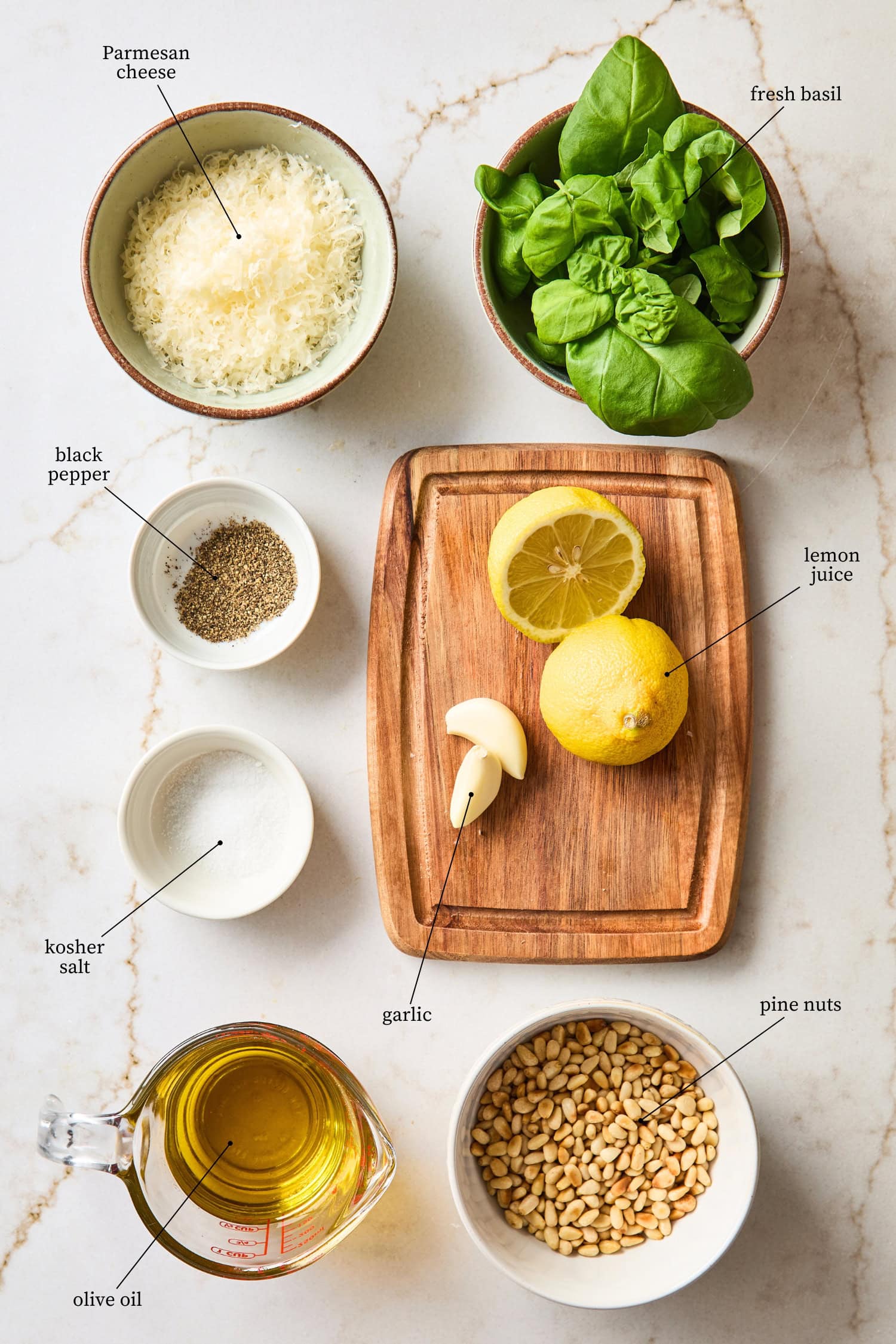 White surface filled with ingredients needed for basil pesto recipe.
