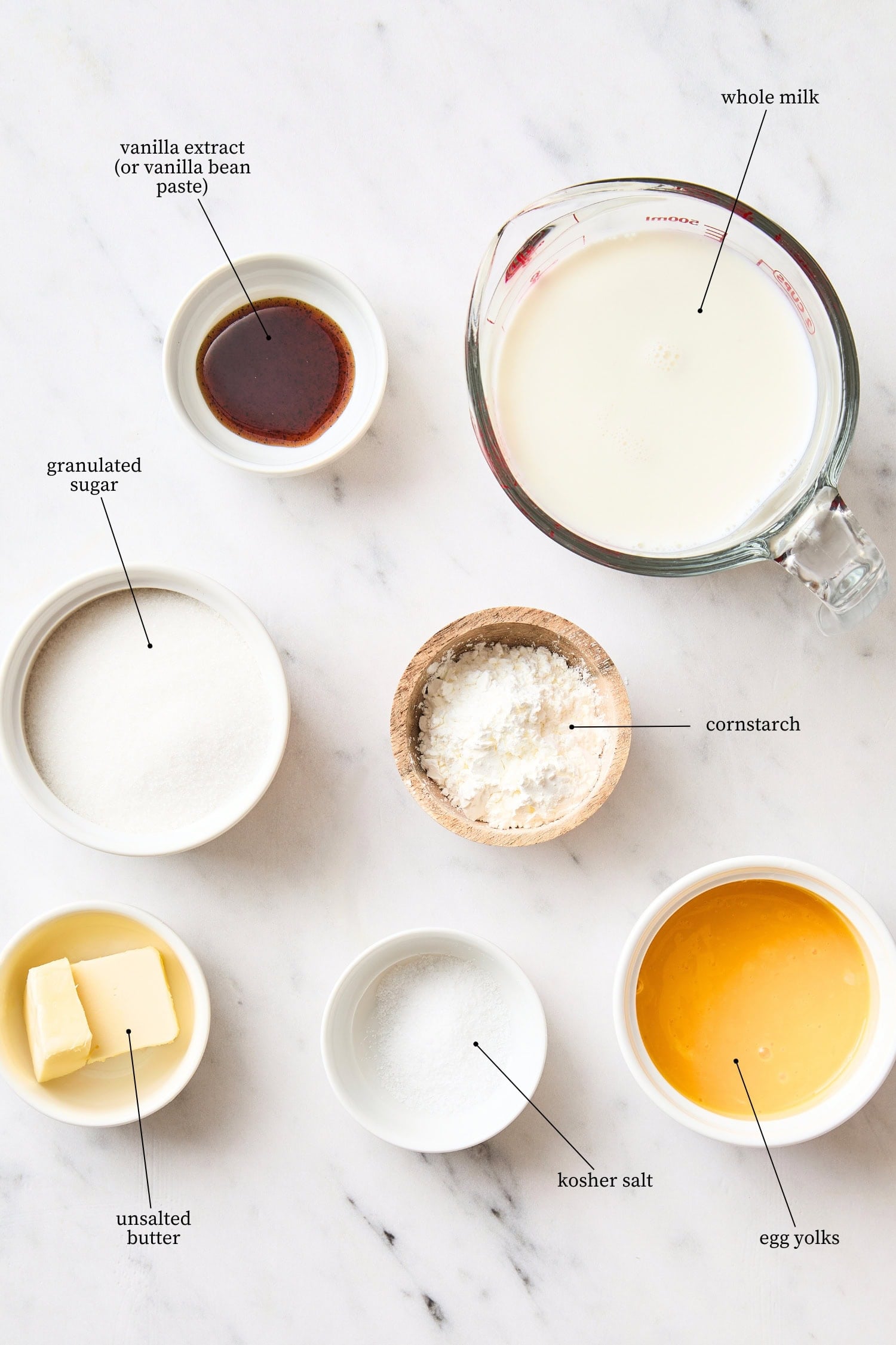 White marble surface filled with ingredients needed for vanilla pudding recipe.