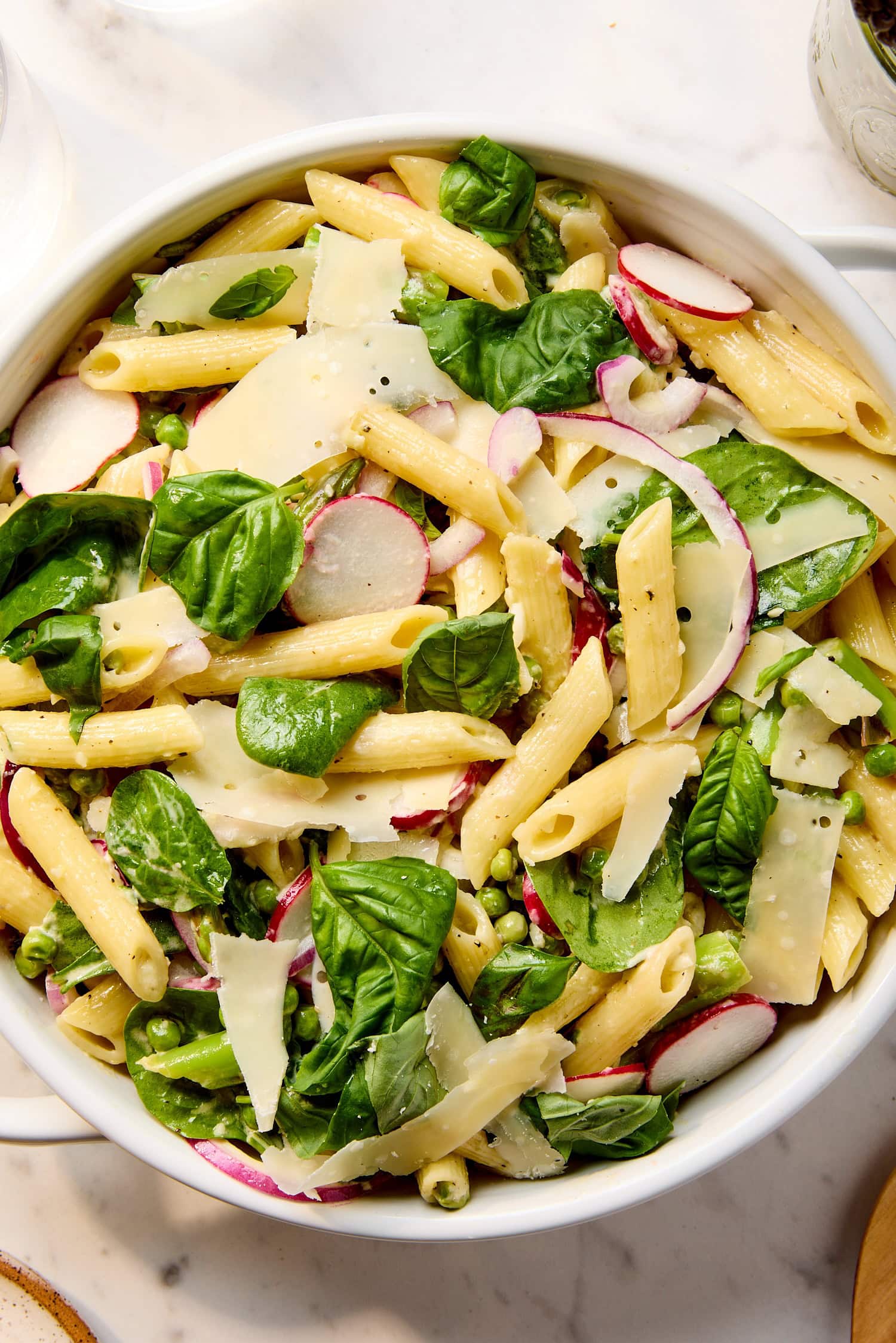 Pasta salad with radish, Parmesan, spinach, red onion, and asparagus in a serving bowl.