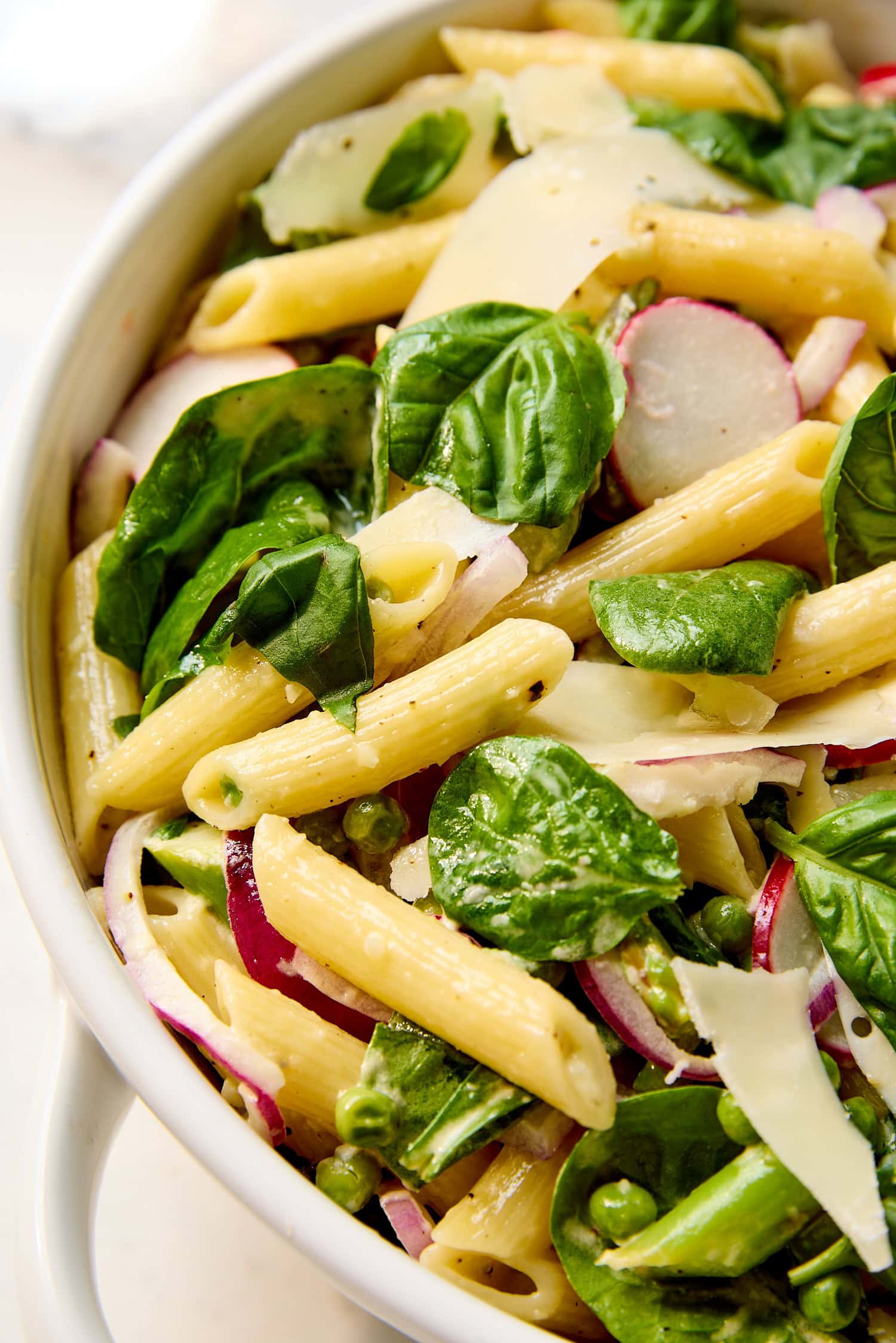 Pasta salad with spinach, radish, peas, and red onion in a serving bowl.