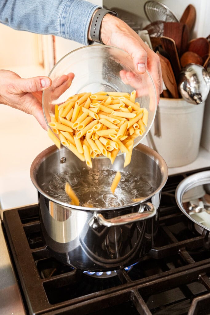Adding penne pasta to a boiling pot of water to cook.