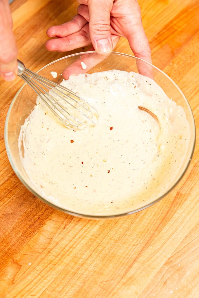 Pasta salad dressing in a bowl on a wooden cutting board.