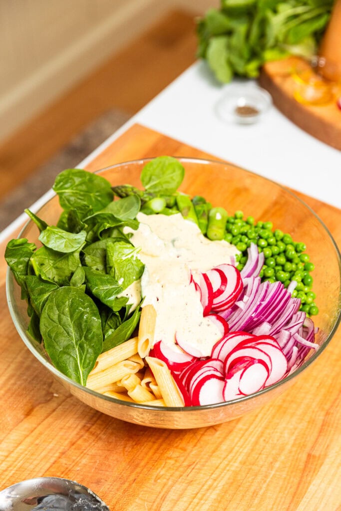 Spinach, radish, onion, peas, asparagus and dressing sit in a bowl prior to being mixed together to form pasta salad.