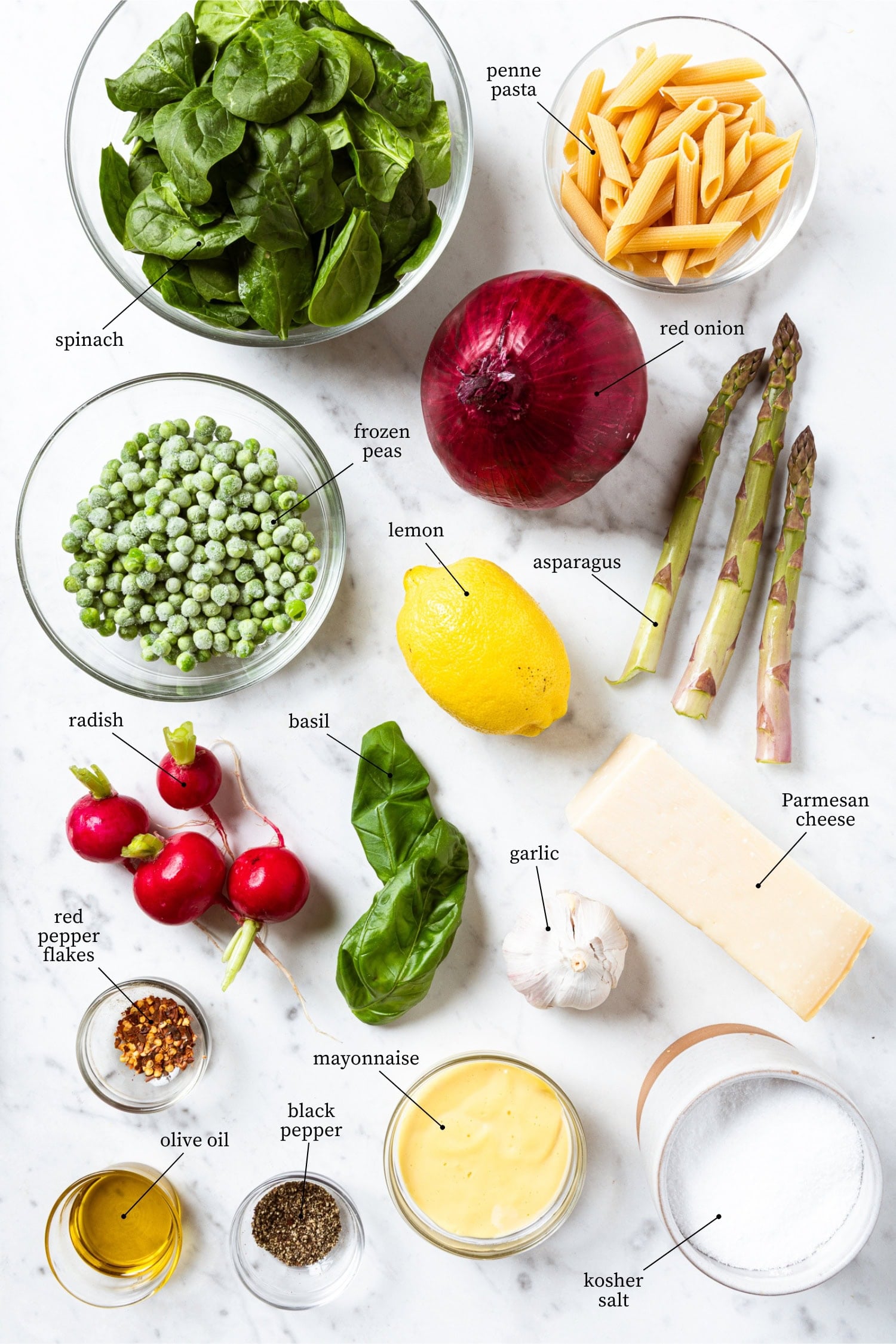White marble surface filled with ingredients for primavera pasta salad including penne, spinach, peas, radishes, and more.