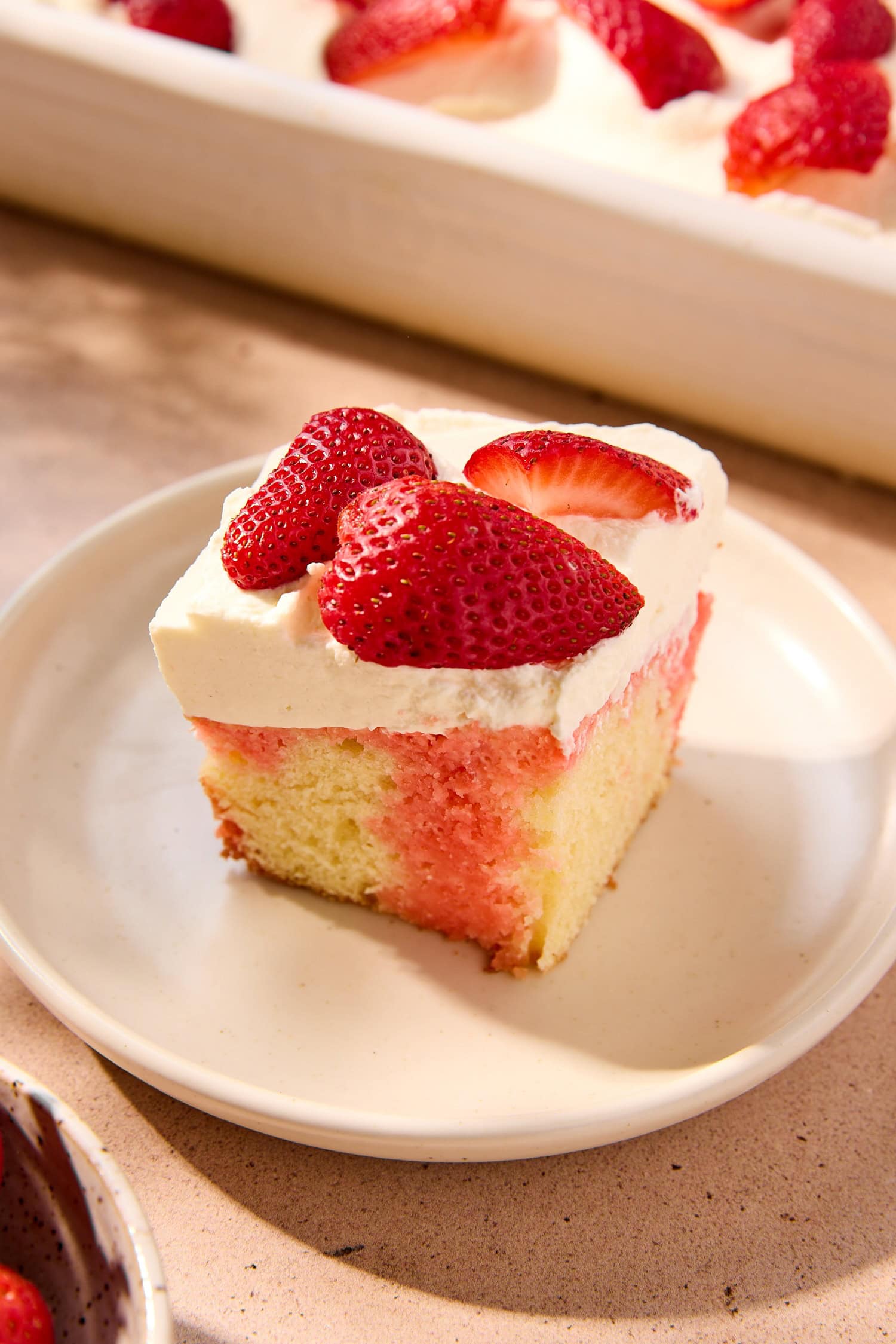 A slice of strawberry poke cake topped with quartered strawberries.