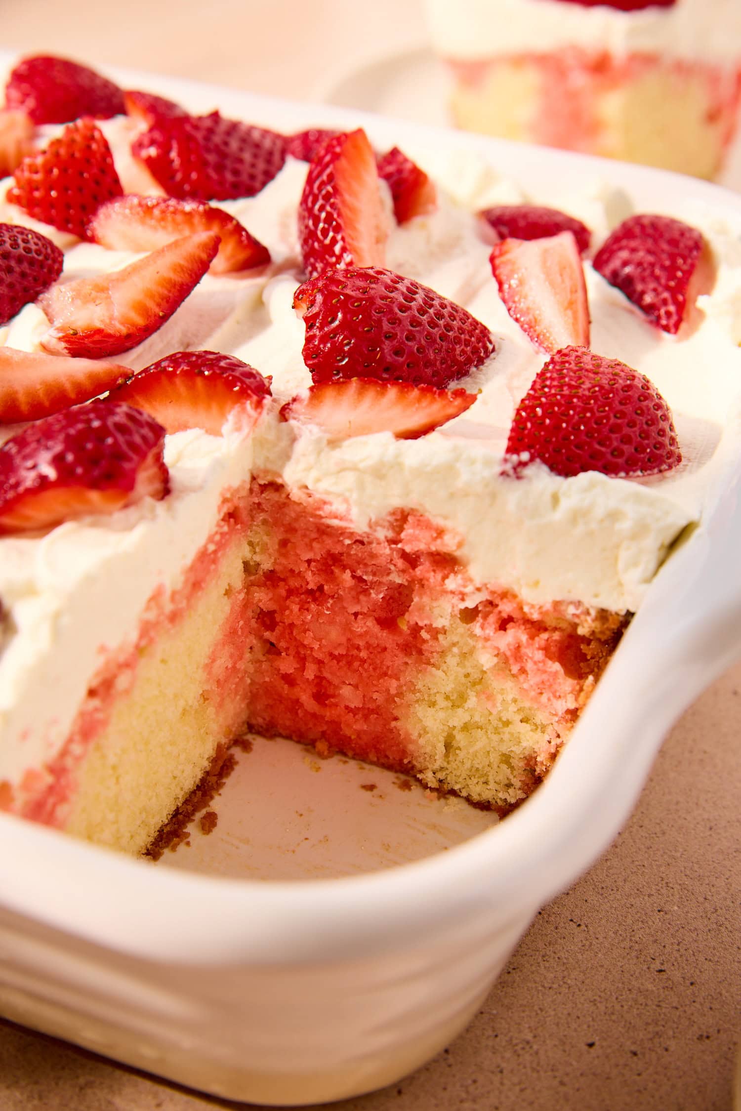 Strawberry poke cake in a dish with a slice missing.