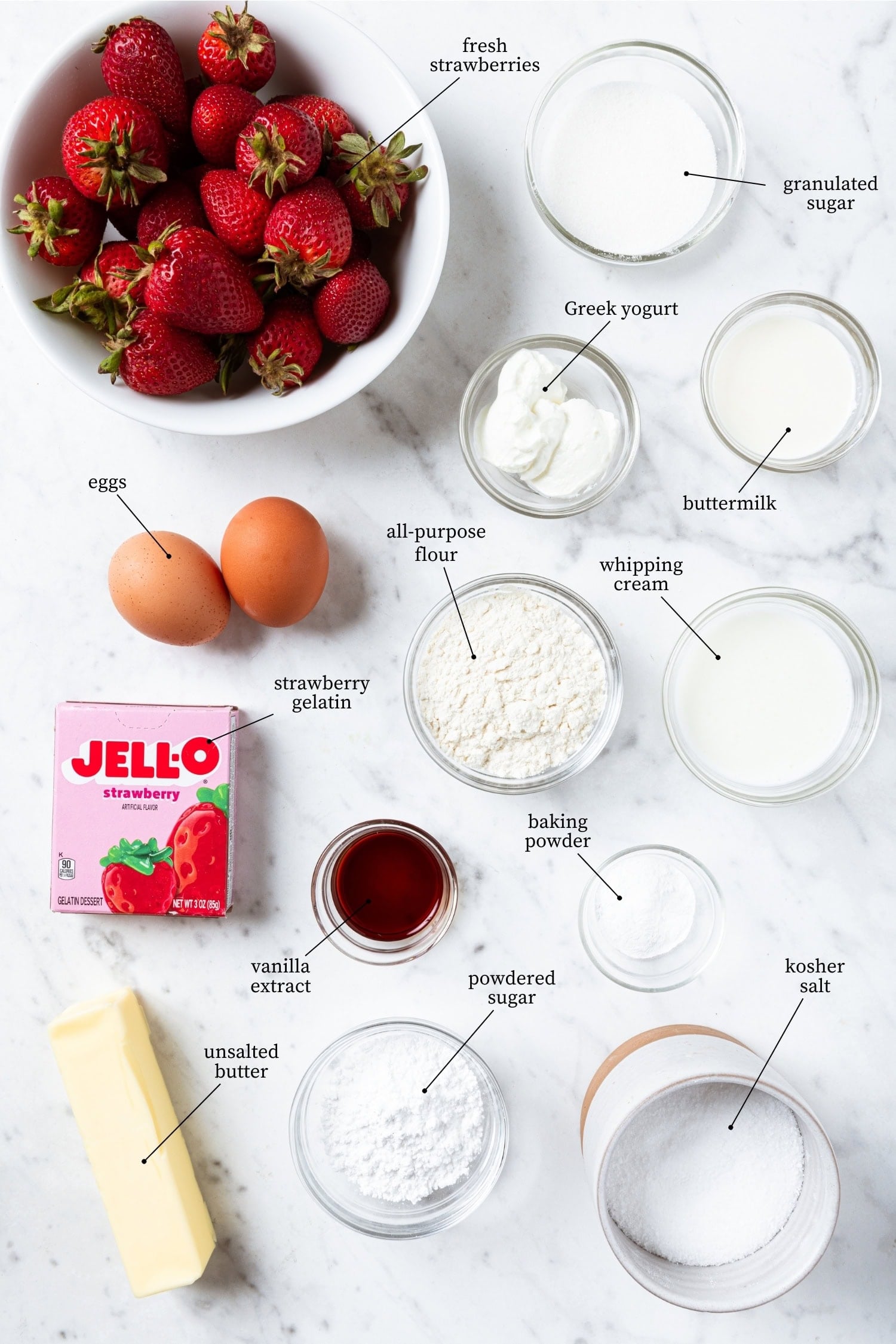 White marble filled with ingredients for strawberry poke cake including Jello, strawberries, flour, and more.