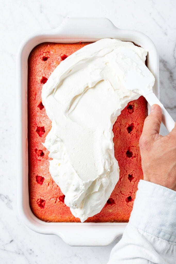 Spreading whipped cream on strawberry poke cake.