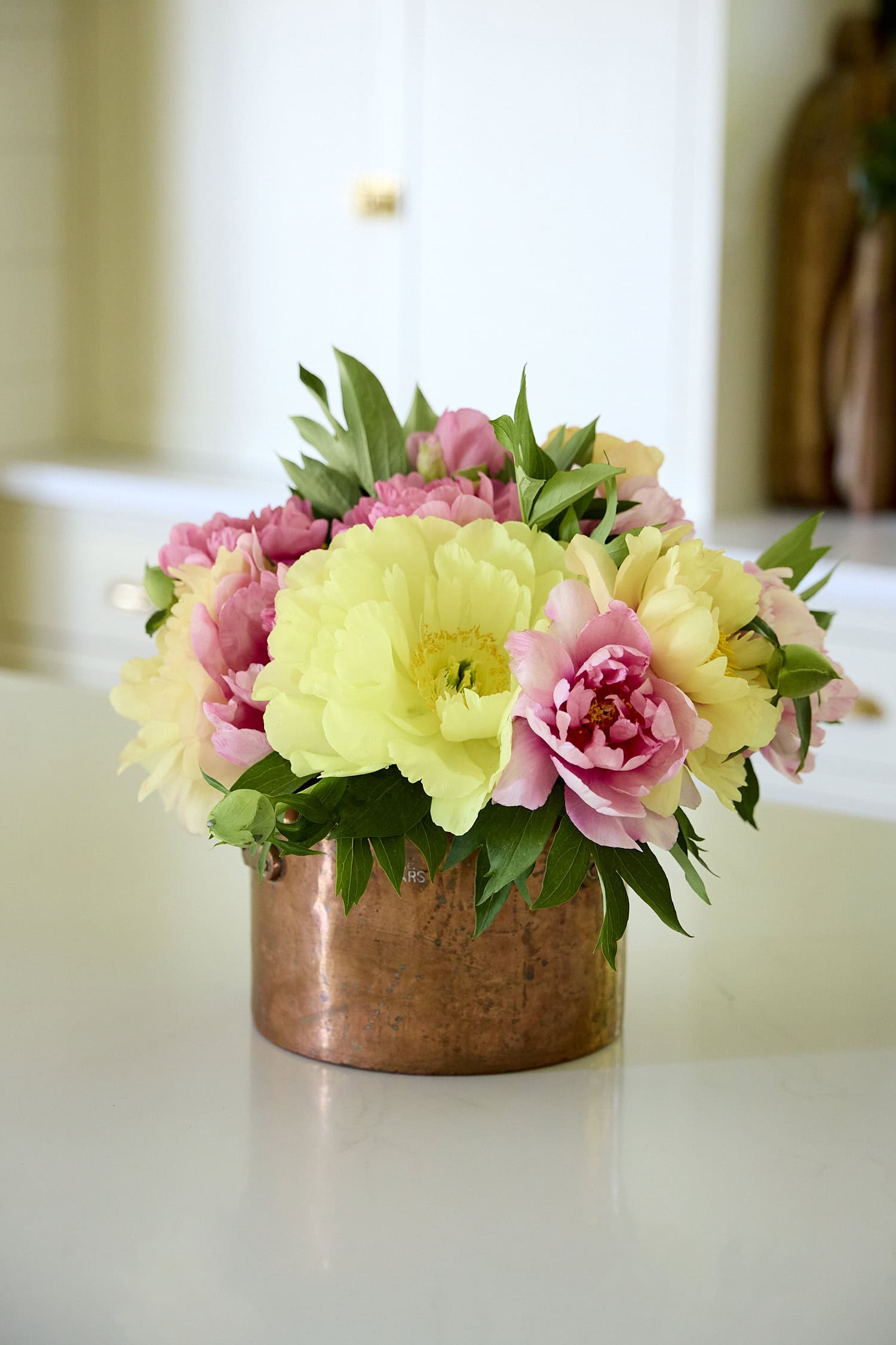 Copper pot filled with Itoh peonies on a kitchen countertop.
