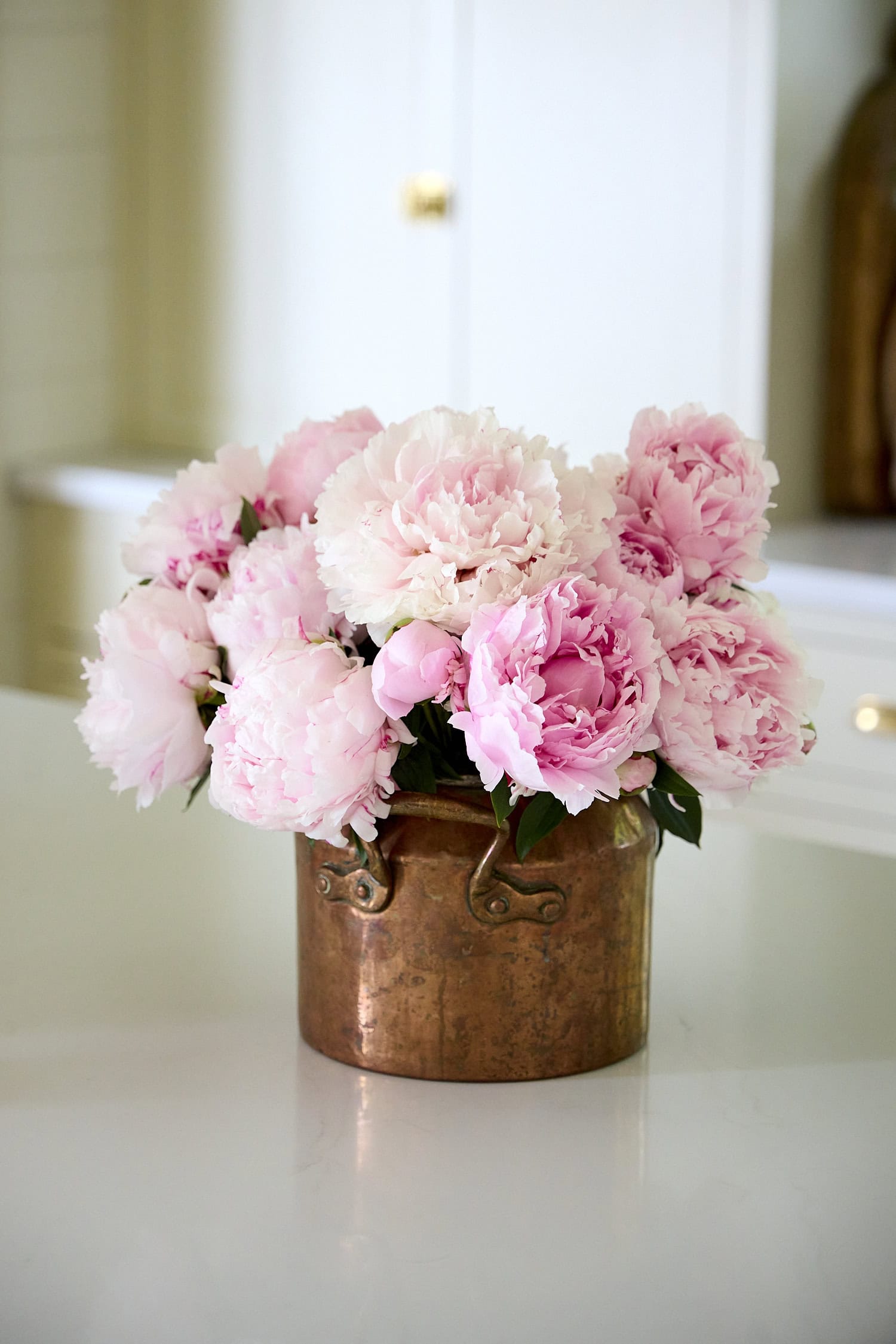 Copper pot filled with pink peonies on countertop.