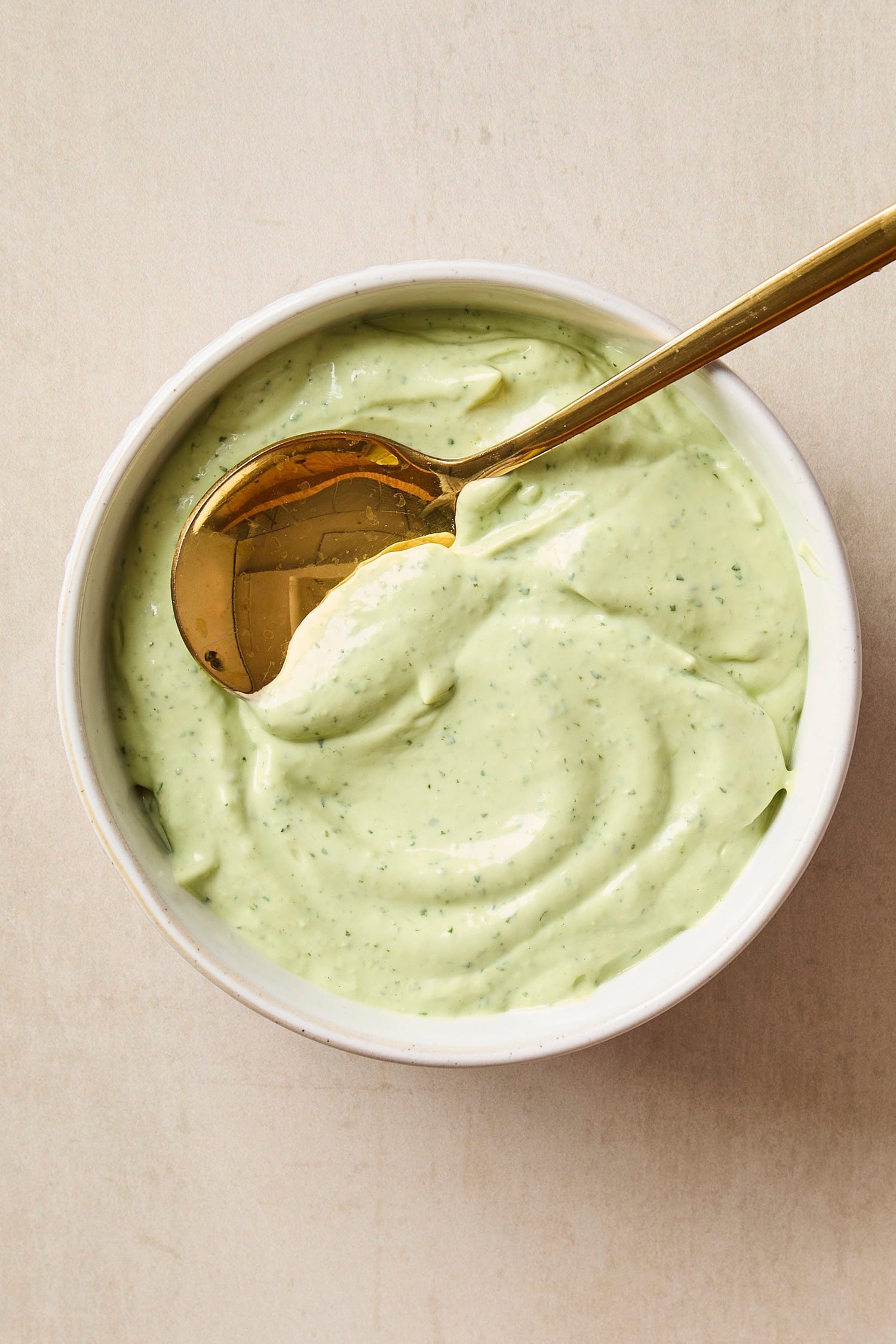 Gold spoon scooping up avocado sauce from a white bowl after being blended.